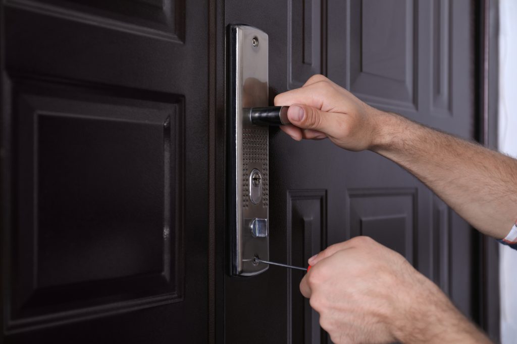 Handyman with screwdriver repairing door lock, closeup